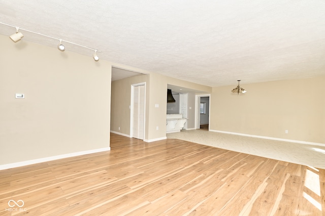 spare room with a chandelier, baseboards, light wood finished floors, and a textured ceiling