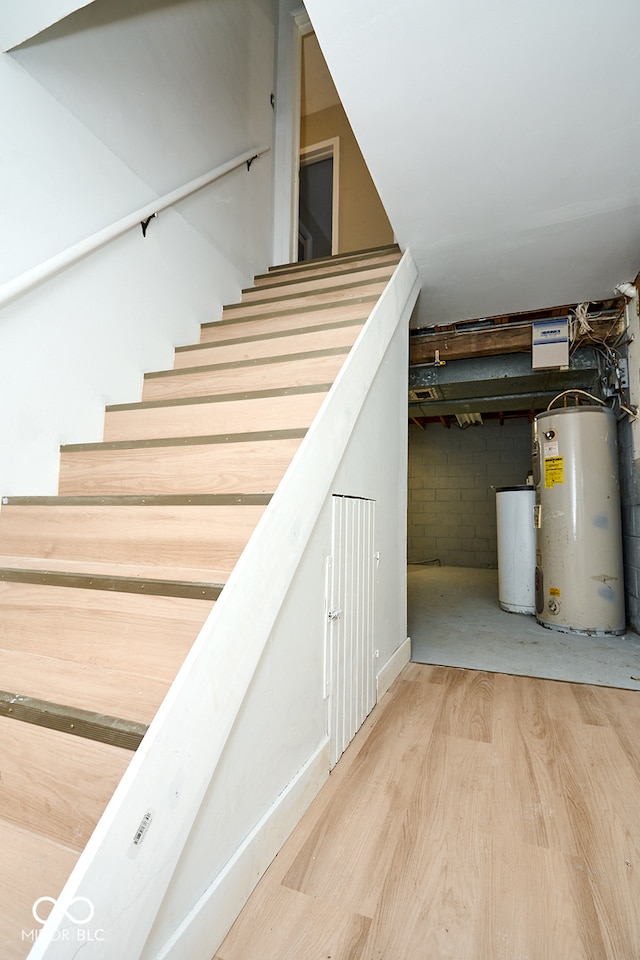 stairs with water heater, concrete block wall, and wood finished floors