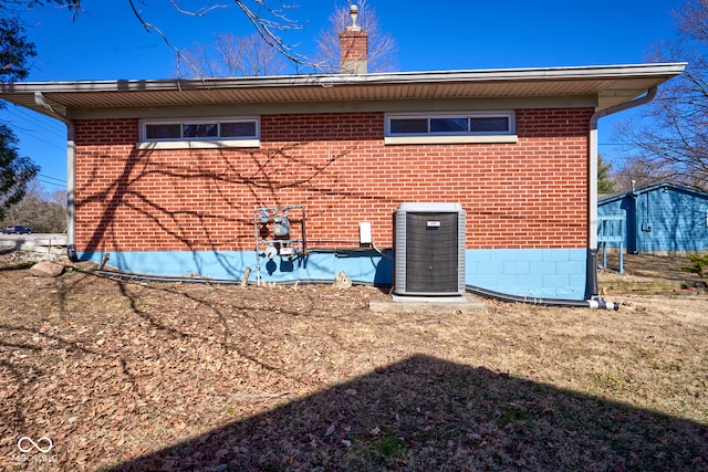 back of house with brick siding, a chimney, and central AC