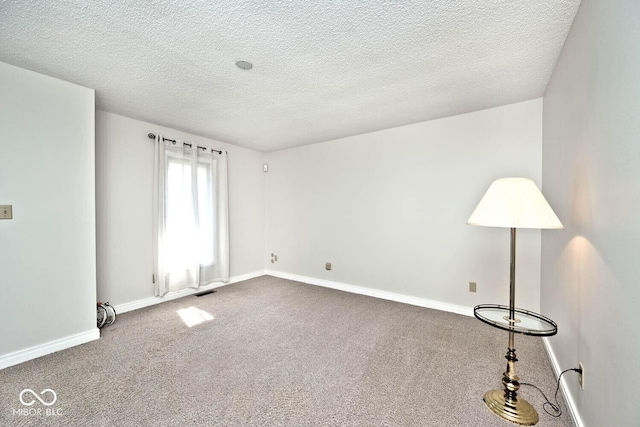 empty room with carpet flooring, a textured ceiling, and baseboards