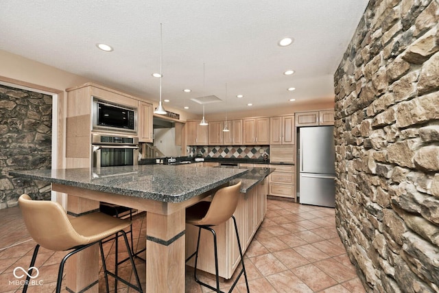 kitchen featuring a breakfast bar, light brown cabinetry, a large island, appliances with stainless steel finishes, and backsplash