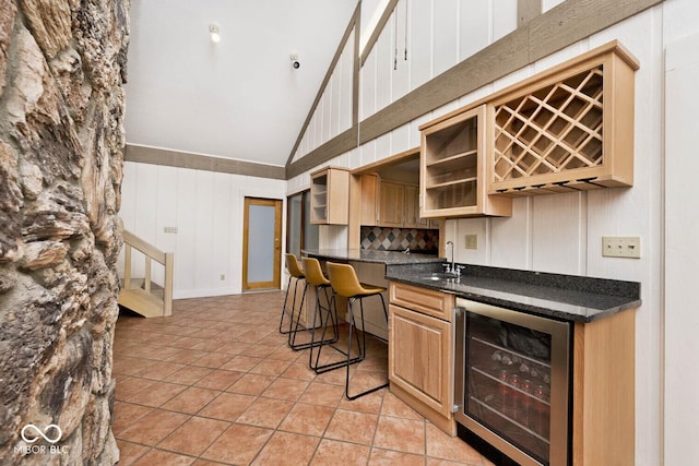 kitchen with high vaulted ceiling, beverage cooler, a sink, light tile patterned flooring, and glass insert cabinets