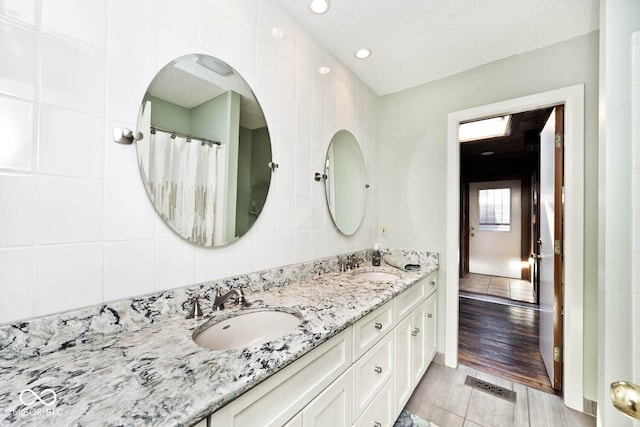 full bathroom with a sink, visible vents, tile walls, and double vanity