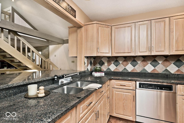 kitchen with light brown cabinetry, dark stone countertops, a sink, backsplash, and stainless steel dishwasher