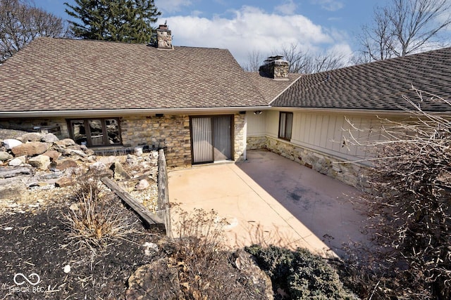 rear view of property with a patio, stone siding, roof with shingles, and a chimney