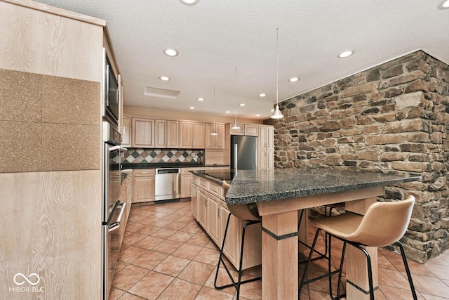 kitchen featuring a breakfast bar area, light brown cabinets, stainless steel appliances, a textured ceiling, and backsplash