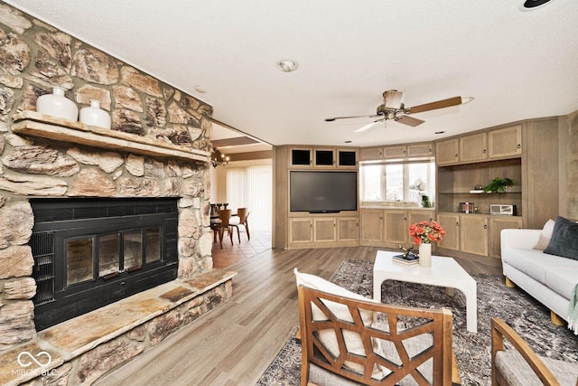 living room featuring a stone fireplace, ceiling fan, and light wood finished floors