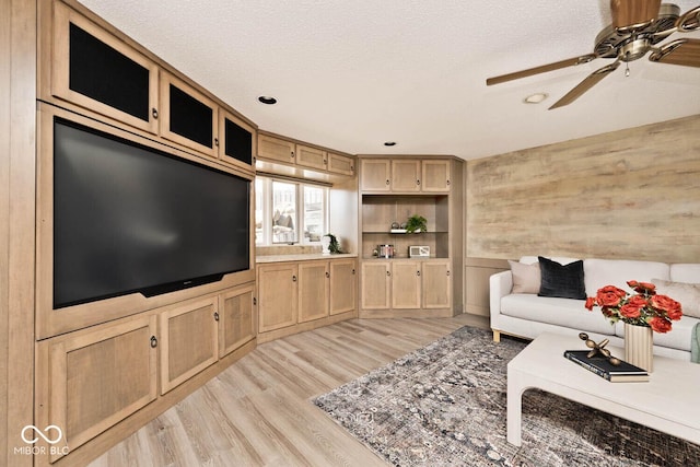 living area featuring a textured ceiling, ceiling fan, wooden walls, and light wood finished floors