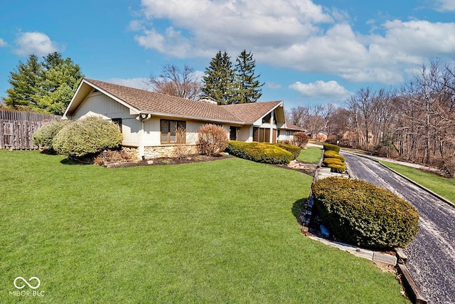 view of home's exterior featuring a yard, fence, stone siding, and a chimney