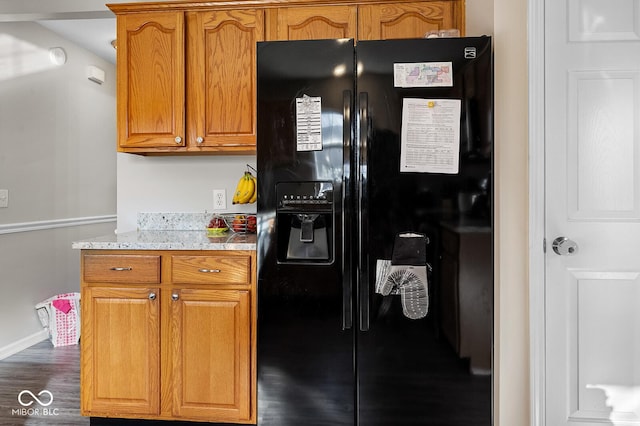 kitchen featuring light stone counters, wood finished floors, baseboards, brown cabinets, and black fridge