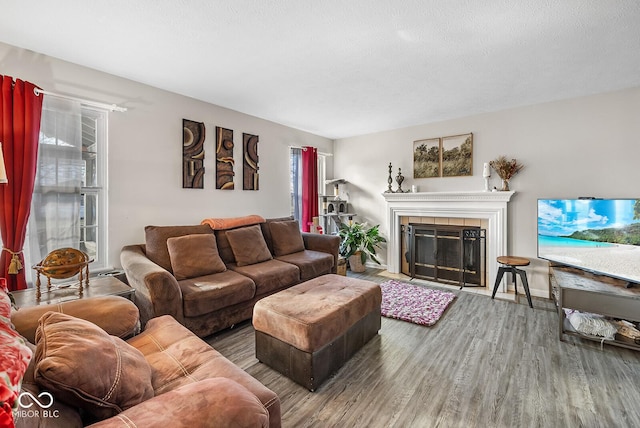 living area featuring a tiled fireplace, a textured ceiling, and wood finished floors