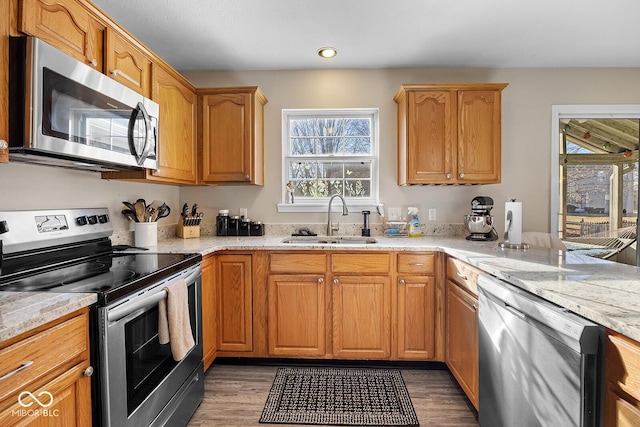 kitchen featuring a sink, stainless steel appliances, light stone counters, and light wood-style floors