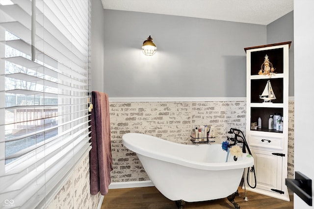 bathroom with a textured ceiling, a freestanding tub, wood finished floors, and wainscoting