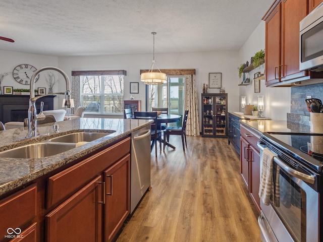 kitchen with a sink, dark stone countertops, tasteful backsplash, appliances with stainless steel finishes, and light wood finished floors