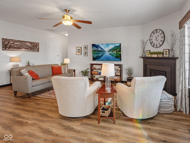 living area with wood finished floors, a glass covered fireplace, and a ceiling fan