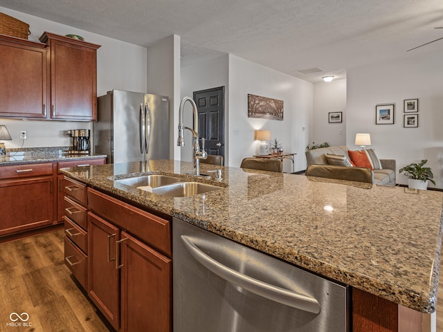 kitchen featuring a sink, dark stone countertops, a textured ceiling, dark wood finished floors, and stainless steel appliances