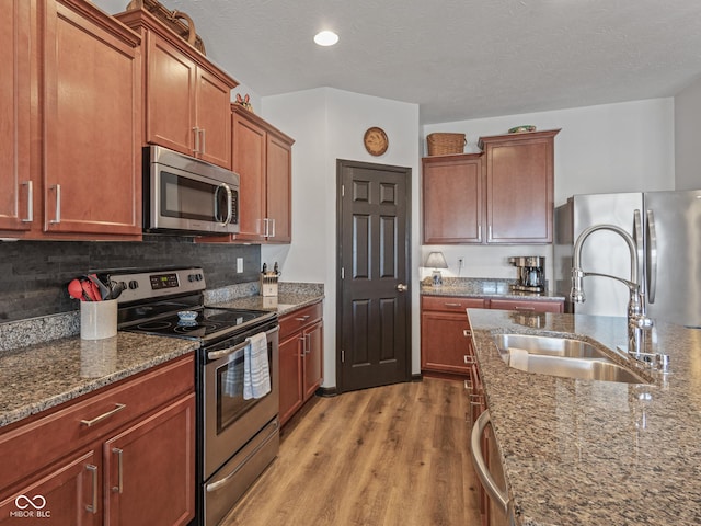 kitchen featuring light wood finished floors, dark stone counters, a sink, decorative backsplash, and appliances with stainless steel finishes