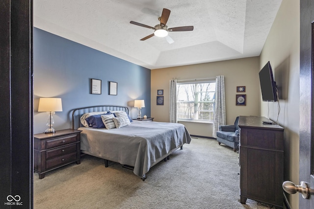 bedroom with a tray ceiling, light colored carpet, ceiling fan, and a textured ceiling