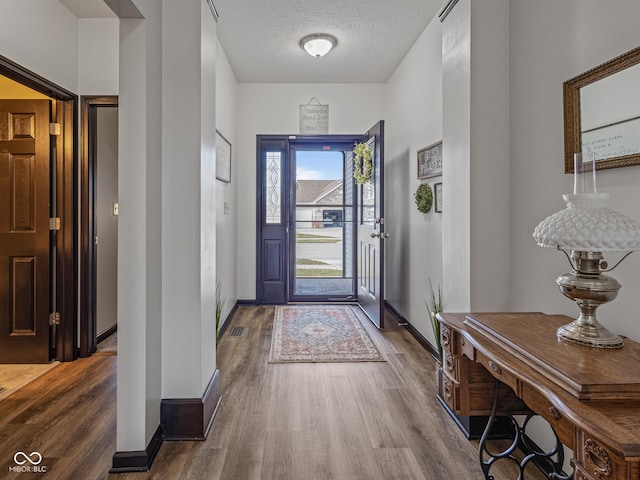 foyer entrance with visible vents, wood finished floors, baseboards, and a textured ceiling