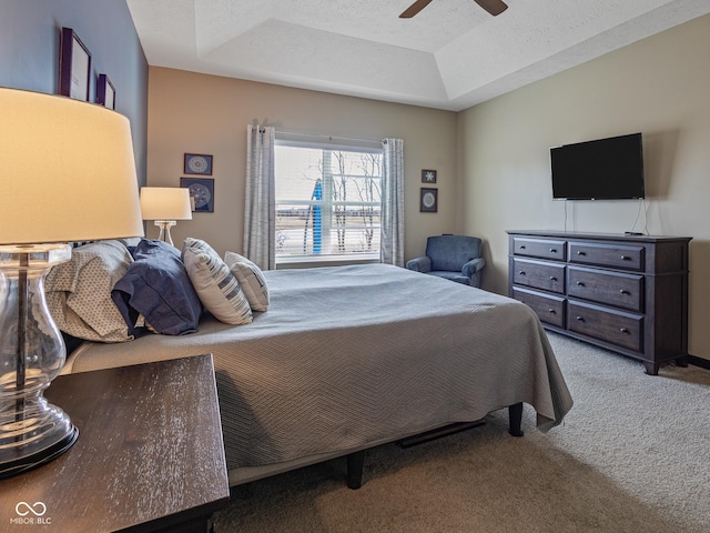 carpeted bedroom with ceiling fan, a tray ceiling, and a textured ceiling