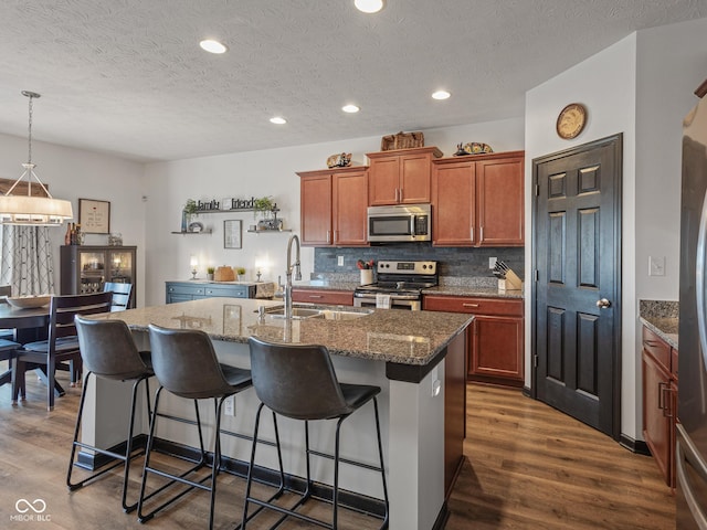 kitchen featuring dark wood-type flooring, a kitchen island with sink, appliances with stainless steel finishes, and a sink