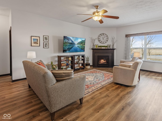 living area with ceiling fan, baseboards, a lit fireplace, and wood finished floors