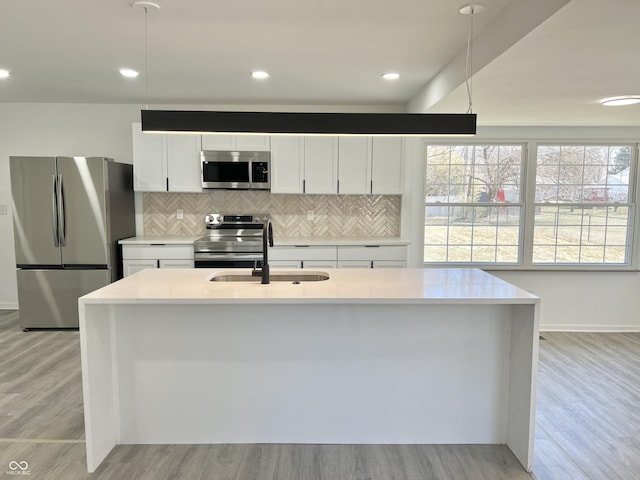 kitchen featuring tasteful backsplash, light countertops, stainless steel appliances, light wood-style floors, and white cabinetry