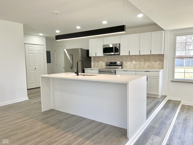 kitchen featuring a center island with sink, stainless steel appliances, white cabinetry, tasteful backsplash, and light wood-type flooring