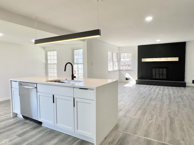 kitchen featuring light wood-type flooring, a sink, stainless steel dishwasher, open floor plan, and light countertops