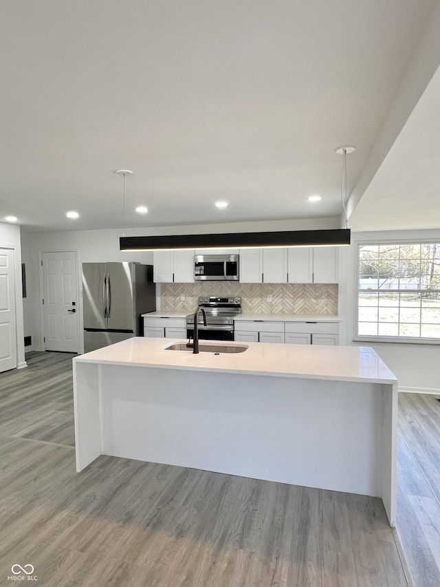 kitchen with light wood finished floors, a sink, stainless steel appliances, light countertops, and white cabinetry