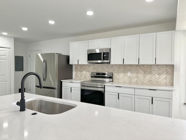 kitchen with tasteful backsplash, light stone counters, stainless steel appliances, white cabinetry, and a sink