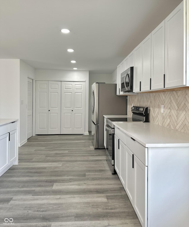 kitchen with light wood finished floors, backsplash, light countertops, appliances with stainless steel finishes, and white cabinets