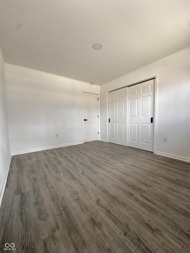 unfurnished bedroom with dark wood-style floors, baseboards, and a closet