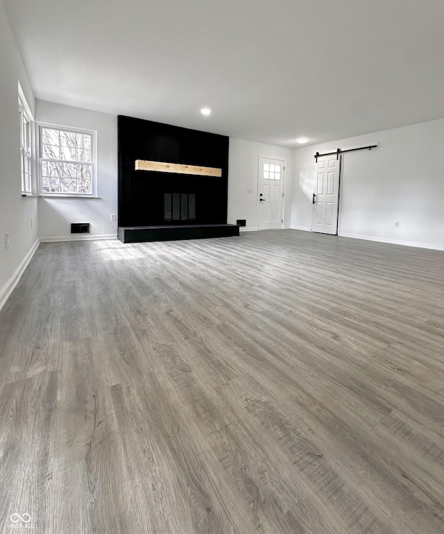 unfurnished living room featuring a barn door, wood finished floors, visible vents, and baseboards