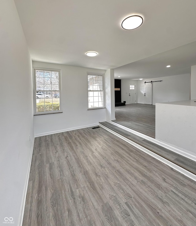 unfurnished room with a barn door, wood finished floors, visible vents, and baseboards