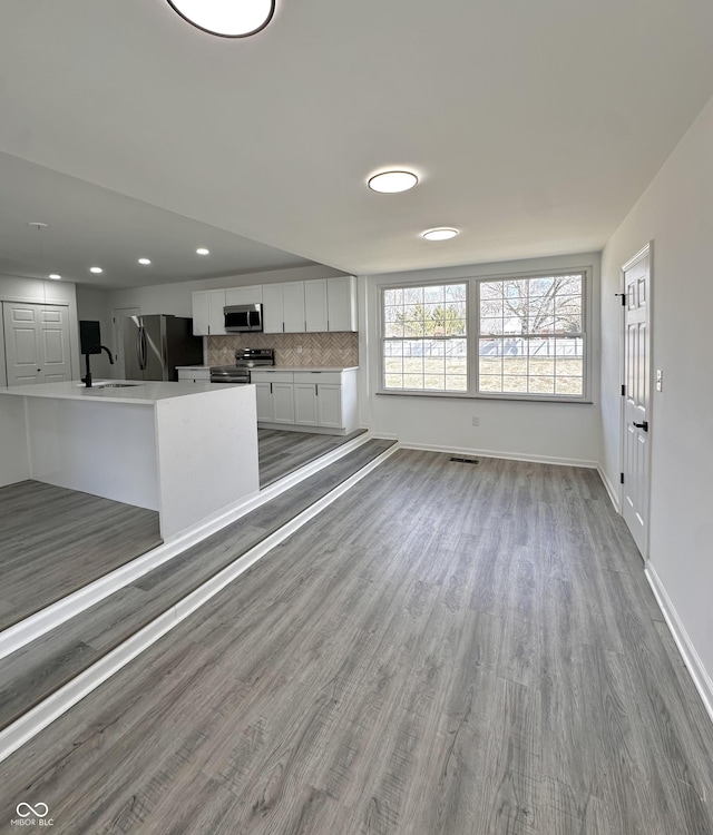 unfurnished living room featuring wood finished floors, visible vents, baseboards, recessed lighting, and a sink