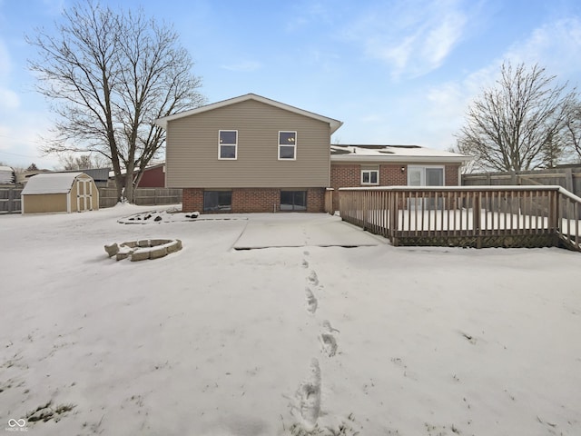 snow covered rear of property featuring a deck, fence, a storage shed, an outdoor structure, and brick siding