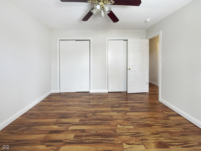 unfurnished bedroom featuring two closets, a ceiling fan, a textured ceiling, wood finished floors, and baseboards