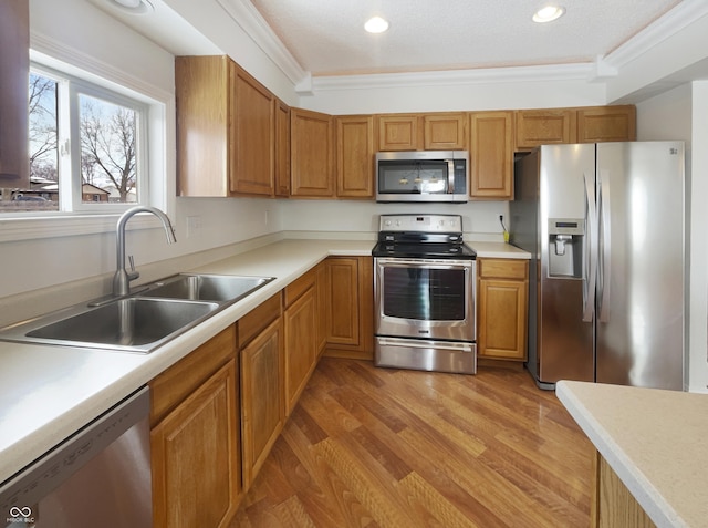 kitchen featuring a sink, light countertops, light wood-style floors, appliances with stainless steel finishes, and crown molding