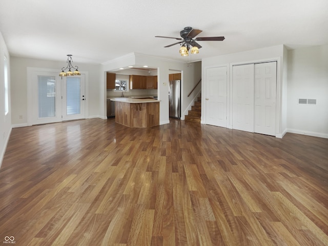 unfurnished living room with visible vents, dark wood-type flooring, ceiling fan with notable chandelier, stairway, and baseboards