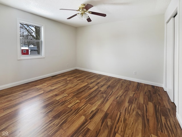 unfurnished bedroom with dark wood-style floors, ceiling fan, a closet, and baseboards