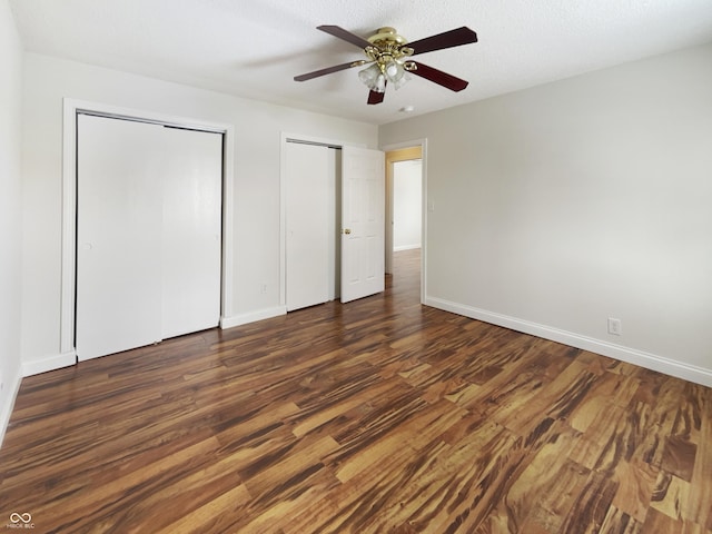 unfurnished bedroom with ceiling fan, wood finished floors, multiple closets, and baseboards