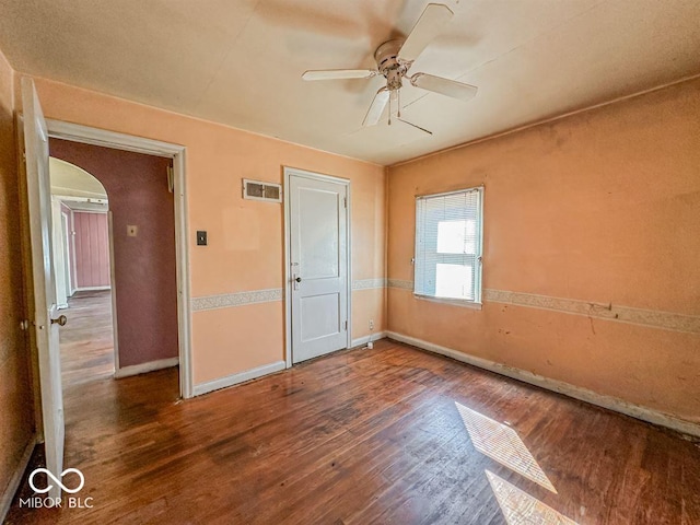 unfurnished bedroom with visible vents, arched walkways, baseboards, and wood finished floors