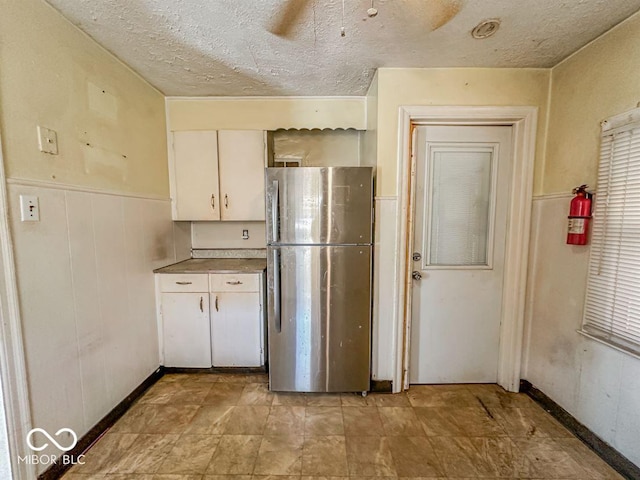 kitchen featuring a ceiling fan, a wainscoted wall, freestanding refrigerator, white cabinets, and a textured ceiling