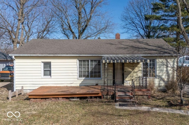 view of front of property with a wooden deck, a chimney, a front lawn, and a shingled roof