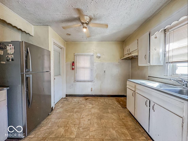 kitchen with a ceiling fan, freestanding refrigerator, a sink, white cabinets, and a textured ceiling