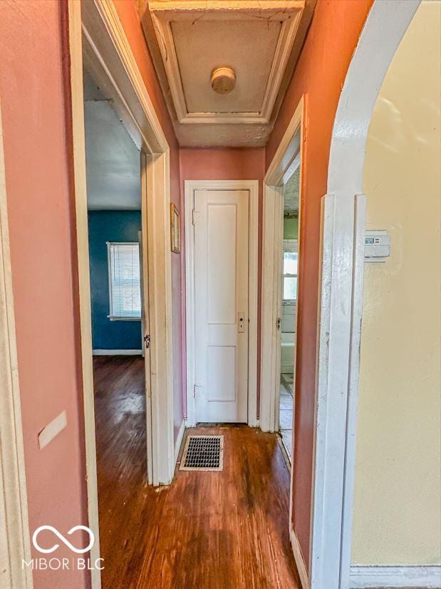 corridor featuring arched walkways, visible vents, baseboards, and wood finished floors