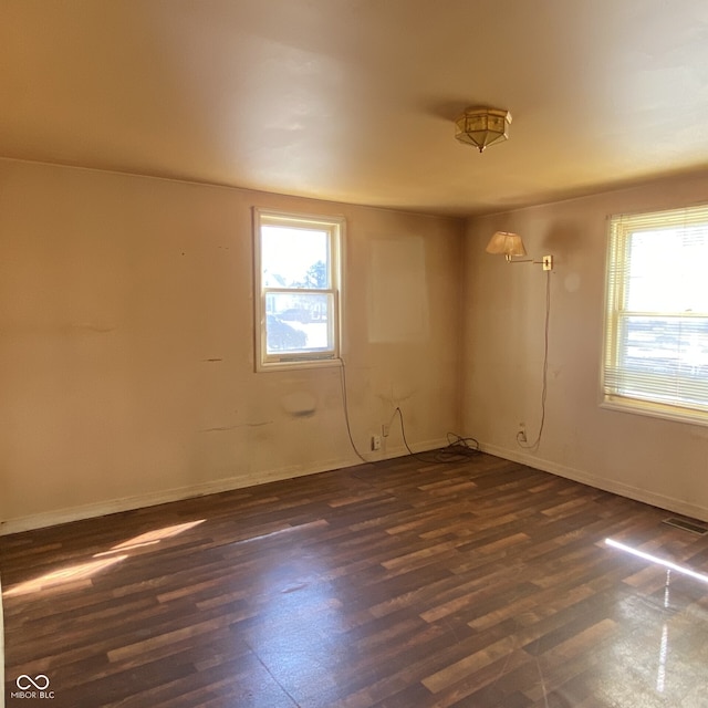 spare room with dark wood-style floors, plenty of natural light, visible vents, and baseboards