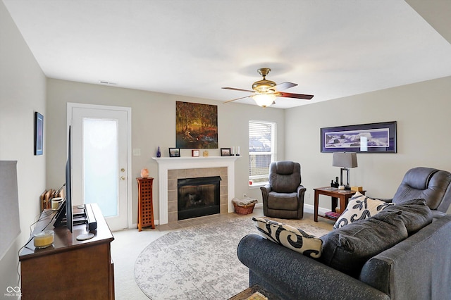 living area featuring visible vents, light carpet, a tiled fireplace, baseboards, and ceiling fan