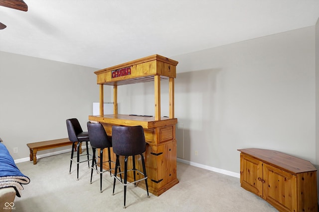 bar with baseboards, light colored carpet, a dry bar, and a ceiling fan